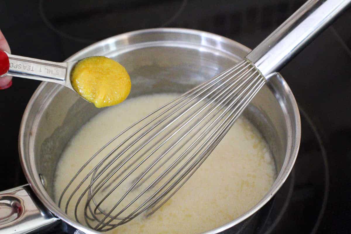 Chicken bouillon paste being added to milk and flour mixture.