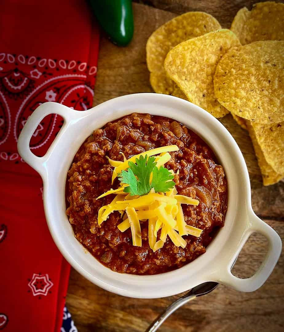 Chili con carne in a white bowl garnished with shredded cheese and cilantro.