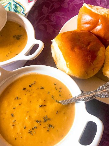 White bowl of soup with a side of dinner rolls