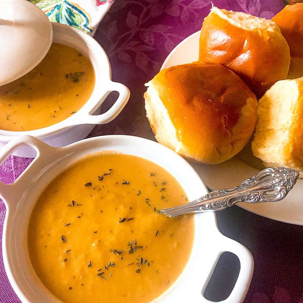 White bowl of soup with a side of dinner rolls