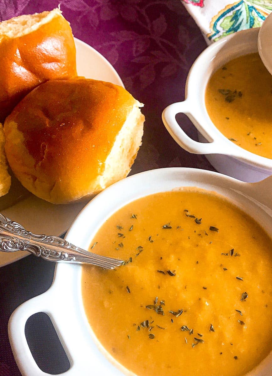 Soup in white bowl with side of dinner rolls.