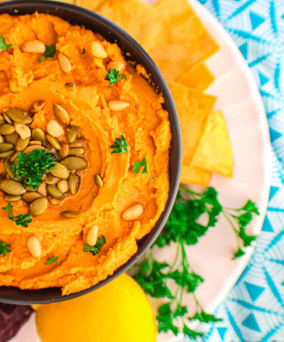 Hummus in a black bowl with a side of chips and a lemon