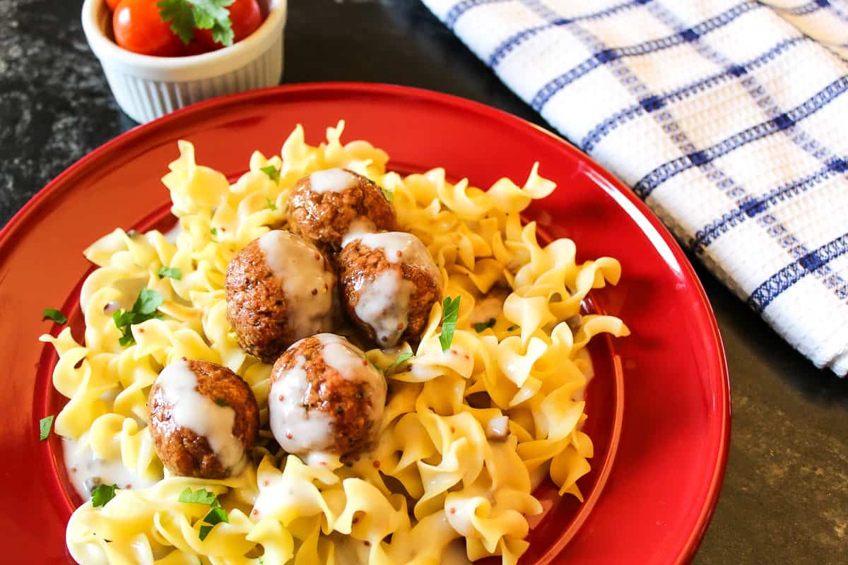 Swedish meatballs and sauce over egg noodles on red plate.