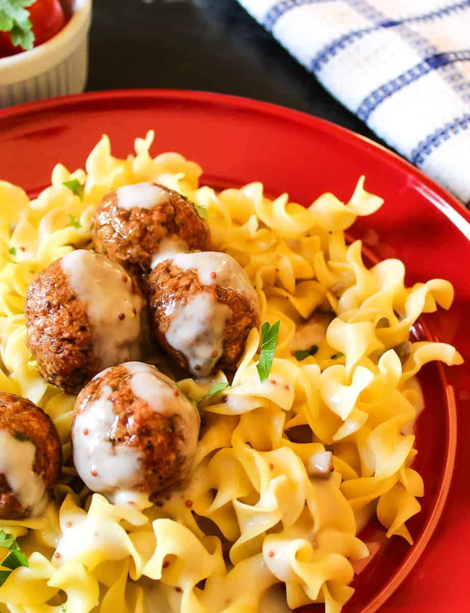 Swedish meatballs with sauce over egg noodles on red plate.