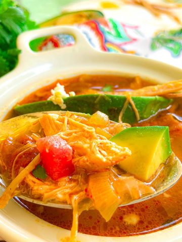 Tortilla soup on a spoon over bowl of soup