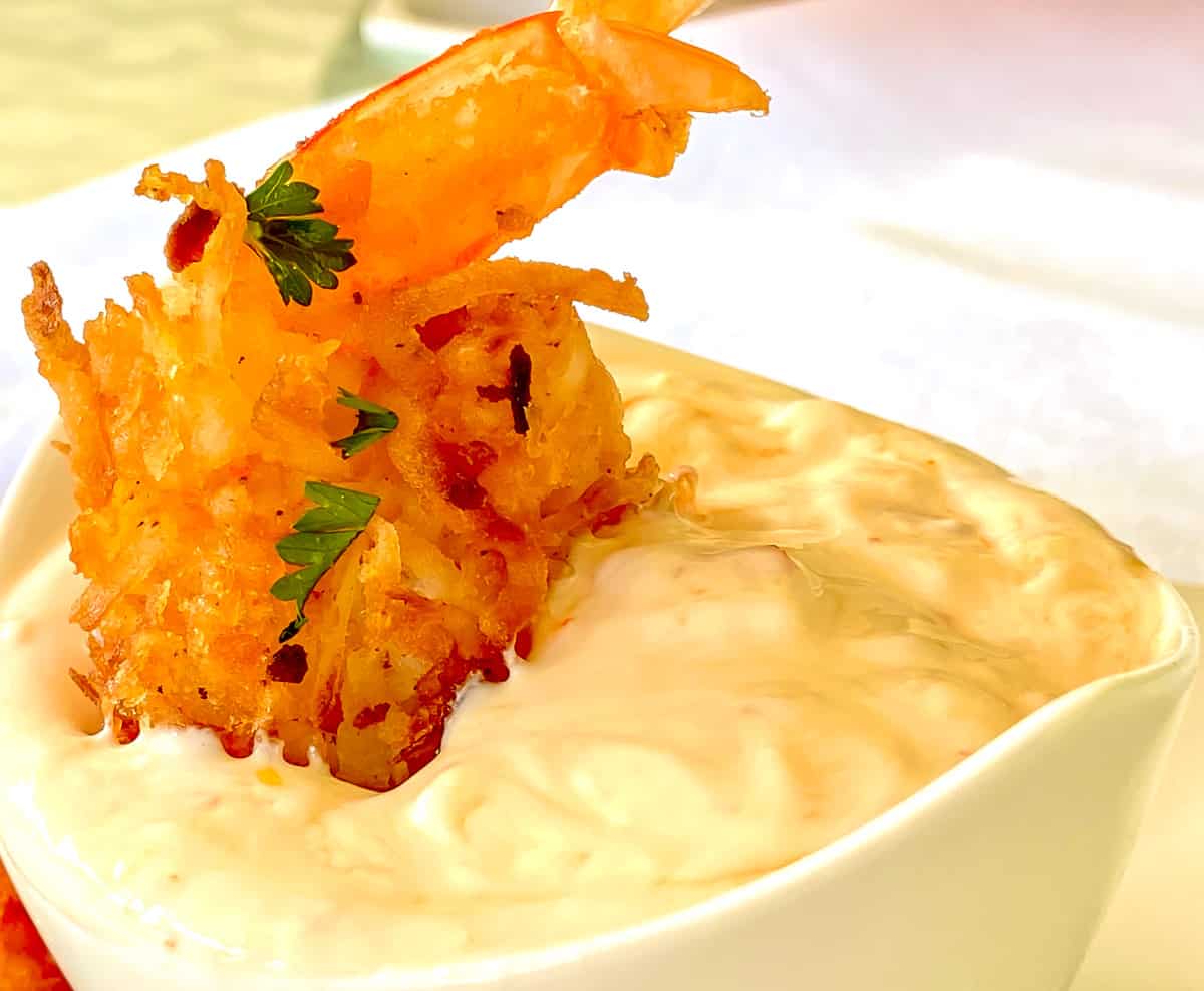 A Coconut shrimp standing up in yogurt dipping sauce.