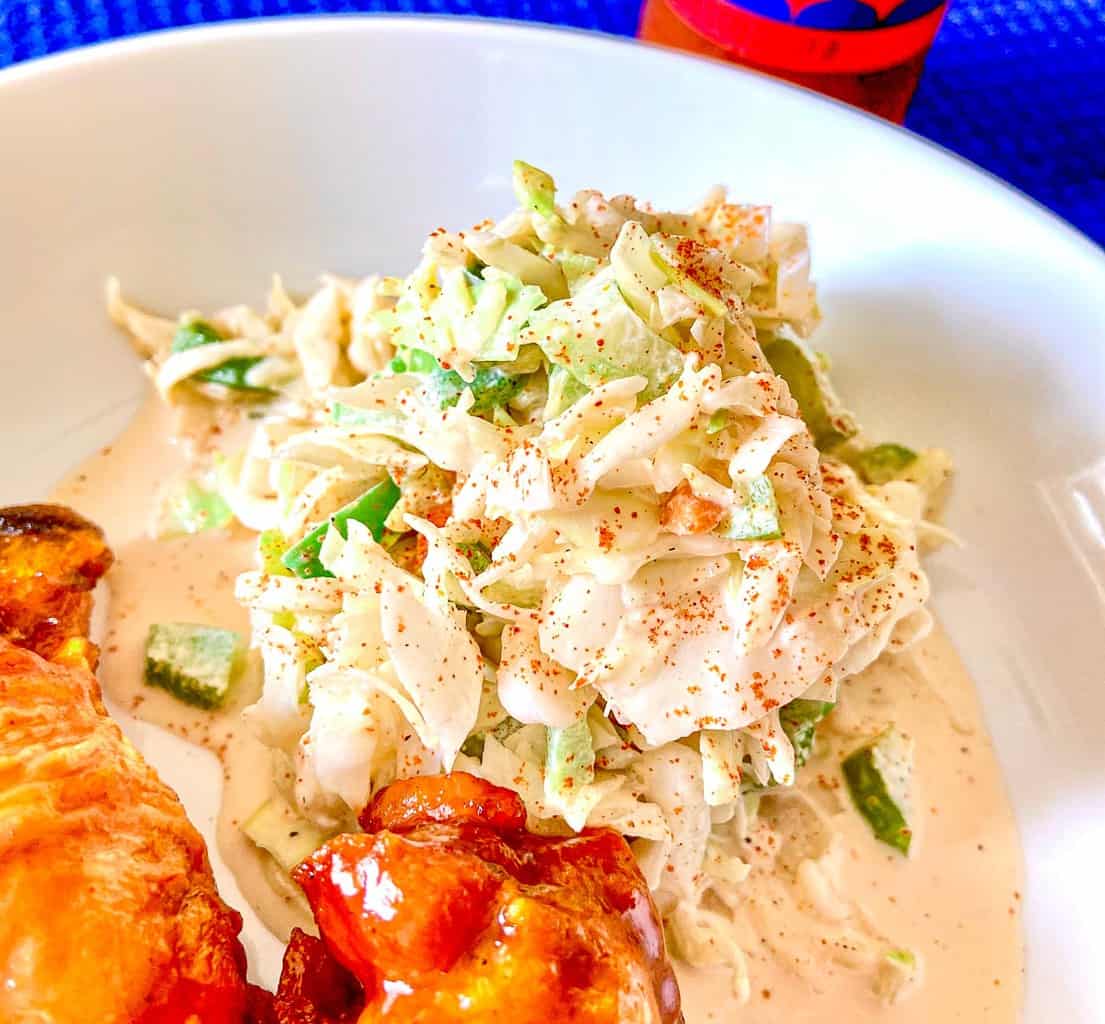 Creamy Creole Coleslaw on white plate with a side of chicken wings