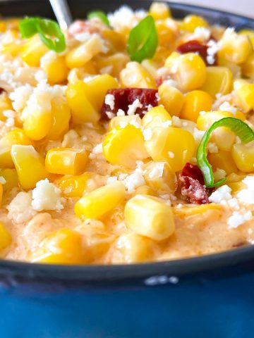 Corn Casserole in black dish garnished with green onion and crumbling cheese