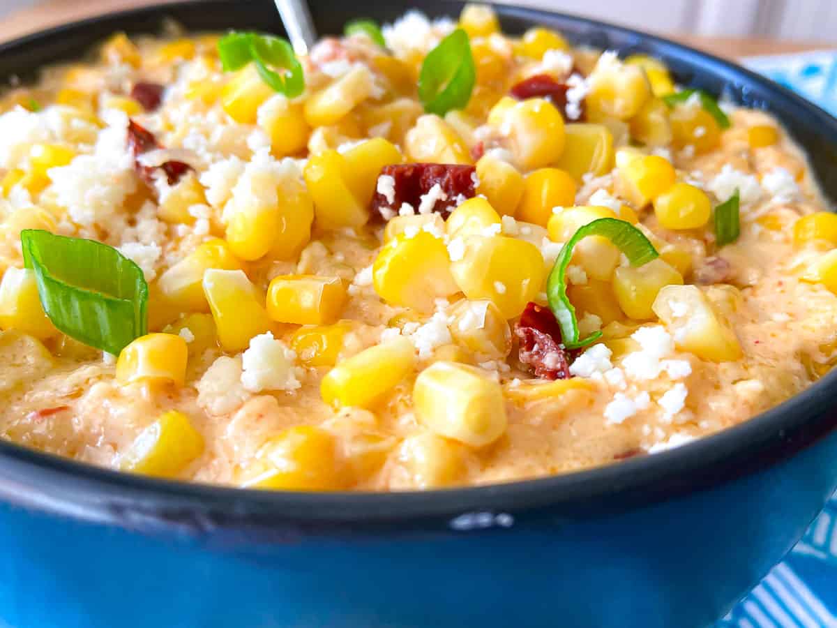 Corn Casserole in black dish garnished with green onion and crumbling cheese