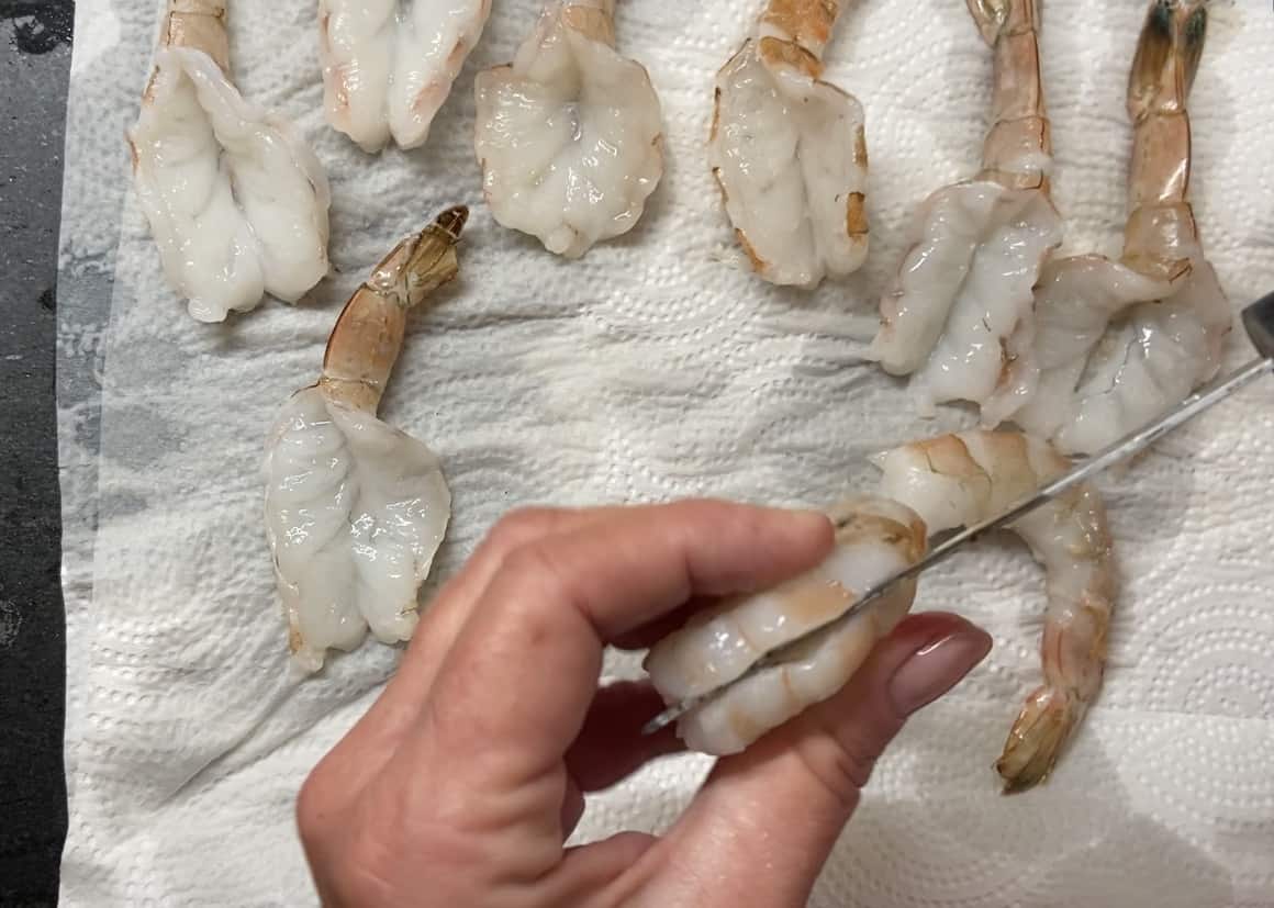 Knife being slid along backside of shrimp.