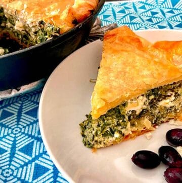 Slice of spinach feta pie on white plate with a side of kalamata olives.