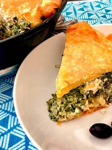 Slice of spinach feta pie on white plate with a side of kalamata olives.