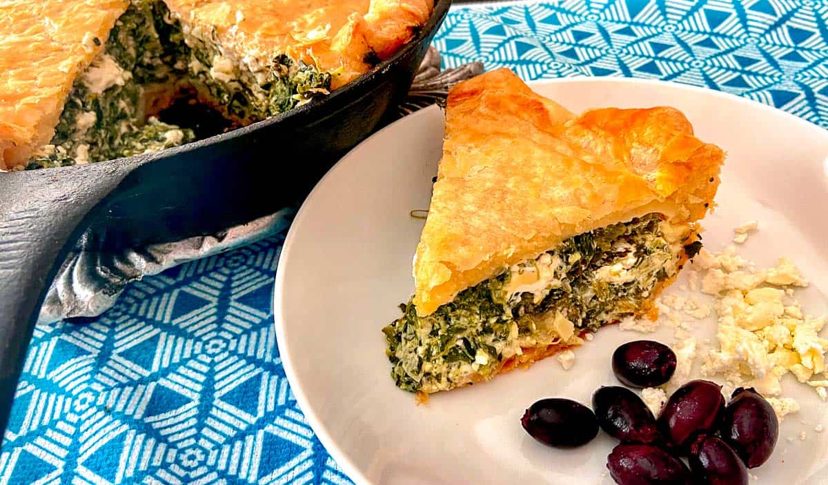 Slice of spinach feta pie on white plate with a side of kalamata olives.