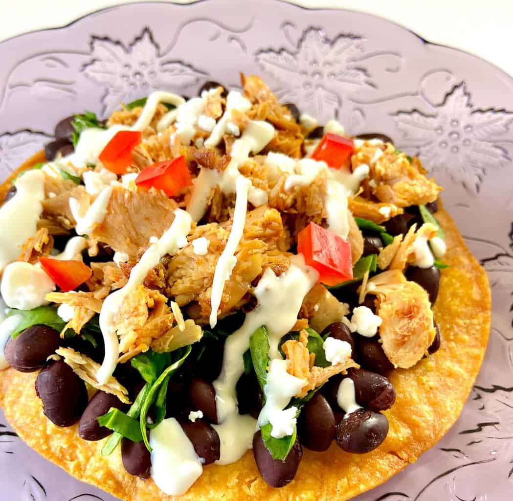 Adobo Chicken on corn tostada with black beans, cilantro and sour cream sauce.