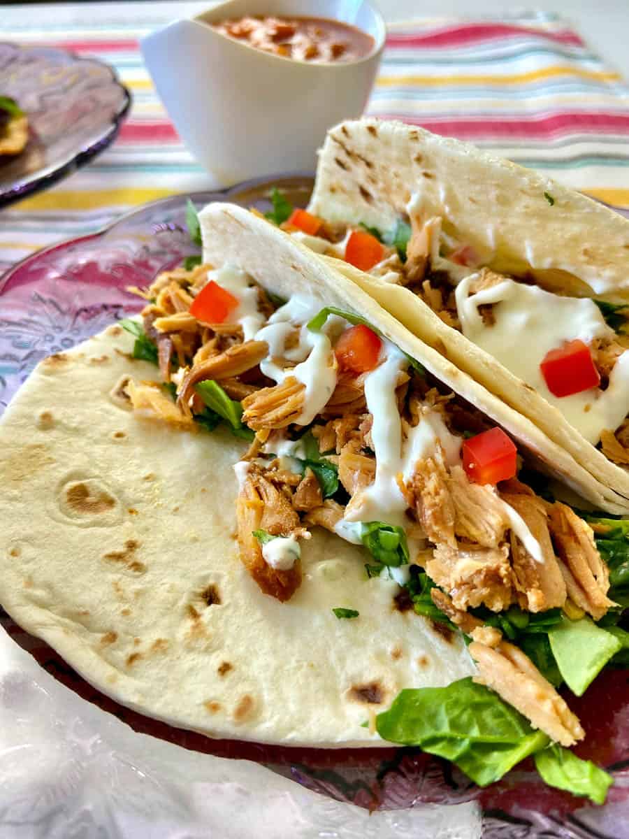 Adobo Chicken on flour tortilla garnished with red pepper and sour cream sauce