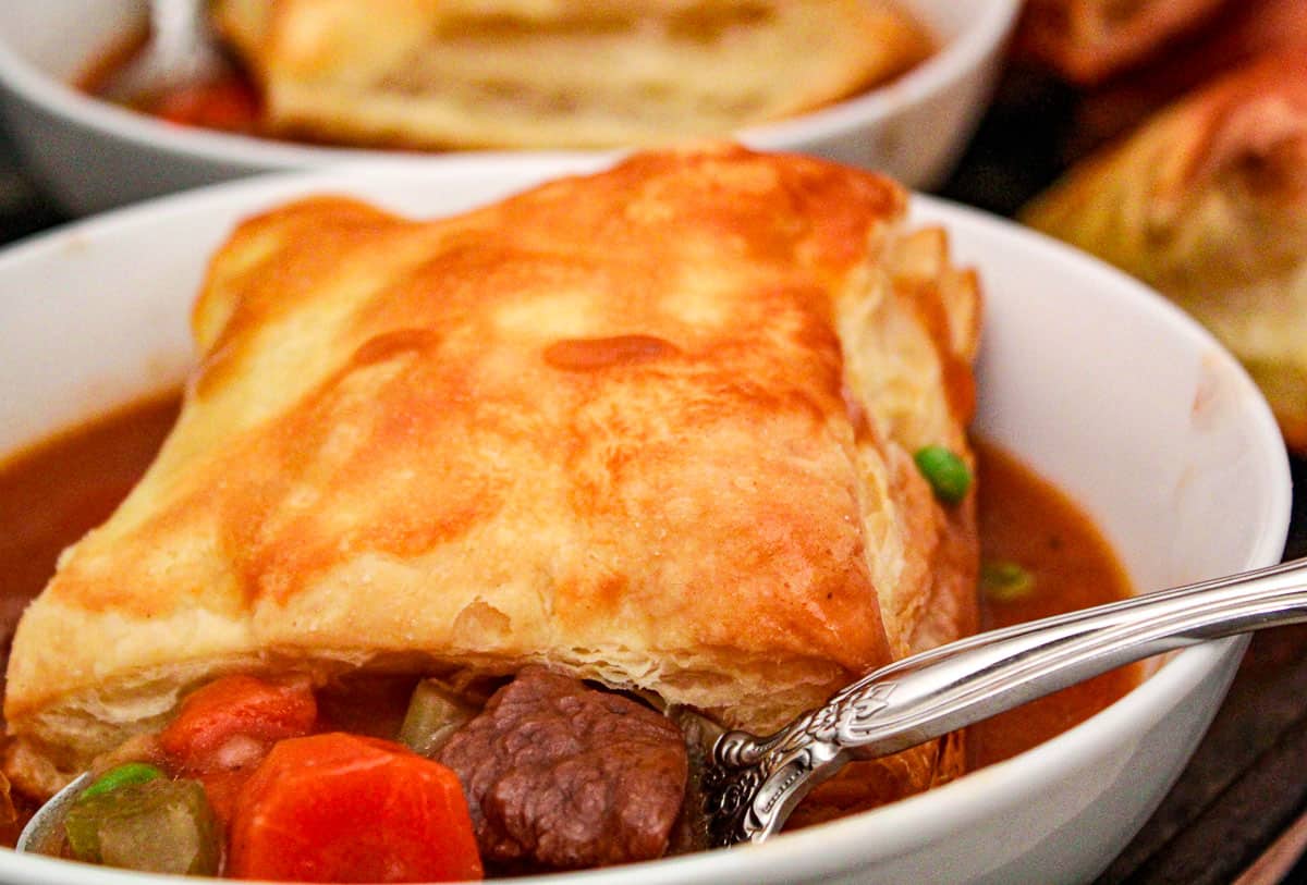 Beef stew in white bowl with a puff pastry on top