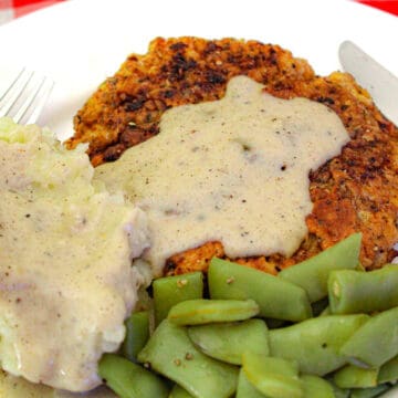 Mashed potatoes, green beans and chicken fried steak with cream gravy on white plate