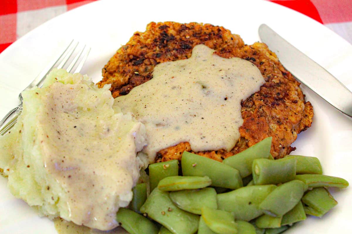 Mashed potatoes, green beans and chicken fried steak with cream gravy on white plate