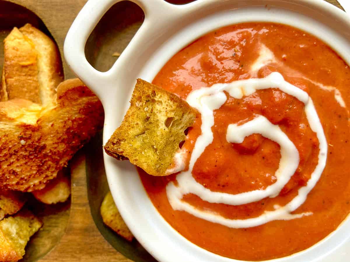 Smoked tomato bisque on brown serving tray with crouton and cream.