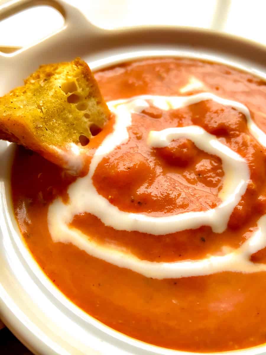 Smoked Tomato Bisque with crouton and a swirl of cream in white bowl.