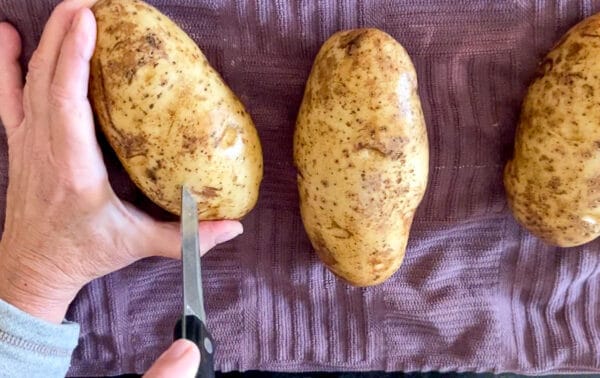 Paring knife cutting slits into russet potato