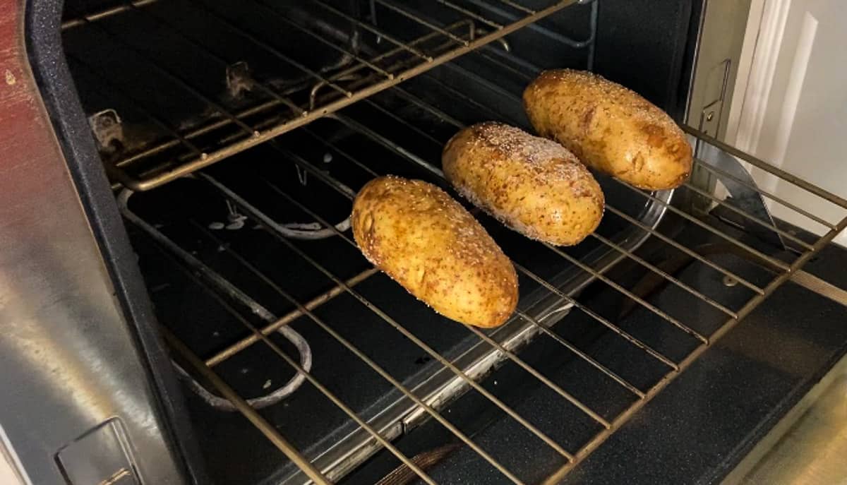 Three oiled and salted potatoes on the middle rack of oven