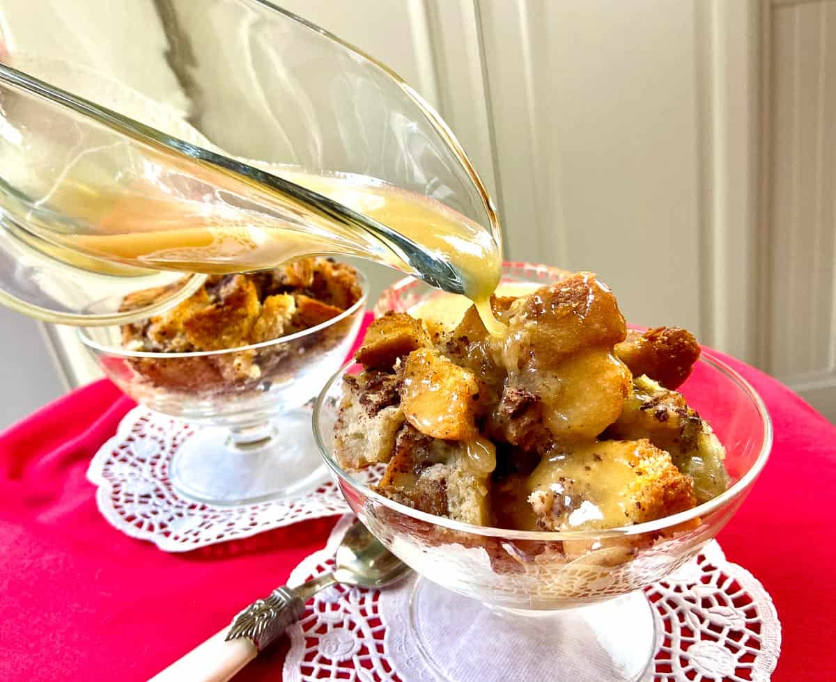 Whiskey sauce drizzled over bread pudding in fluted glass bowl.