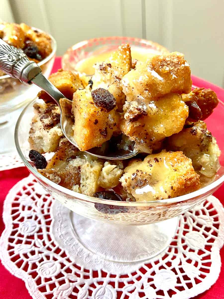 A spoonful of bread pudding with raisings in glass bowl on white doile.