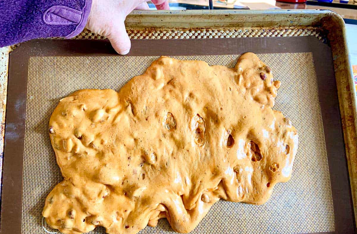 Baking pan being tilted with brittle batter on it.