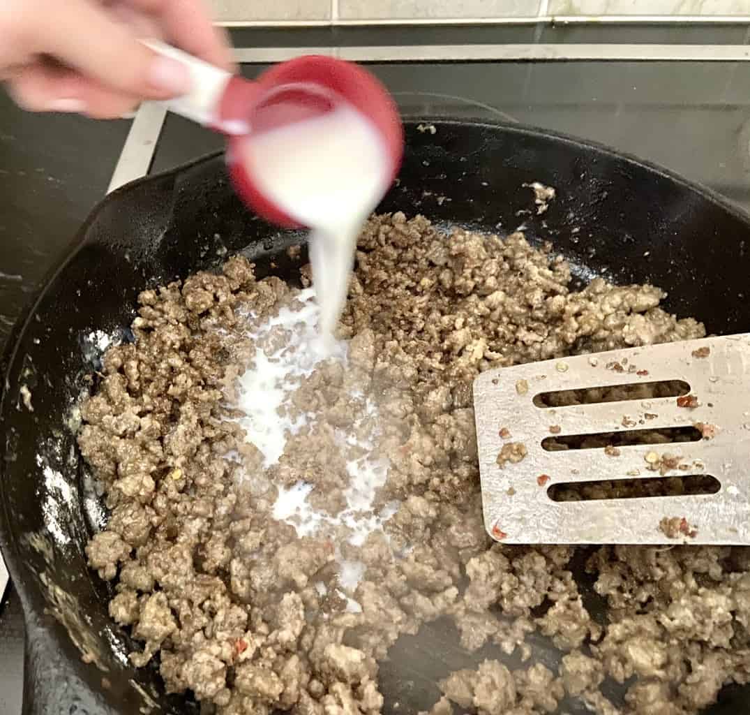 Milk being added to cooked sausage and flour