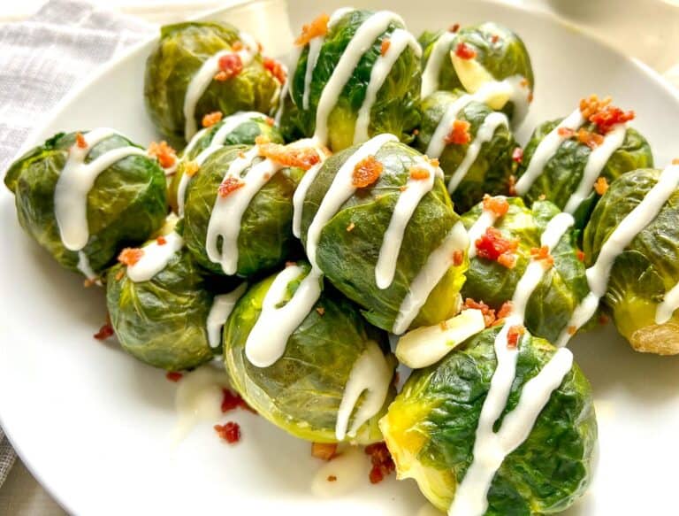 White bowl of Brussels Sprouts drizzled with Horseradish cream sauce and garnished with bacon bits