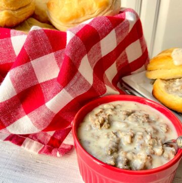 Sausage cream gravy in red bowl with bowl of biscuits in red checkered basket in background