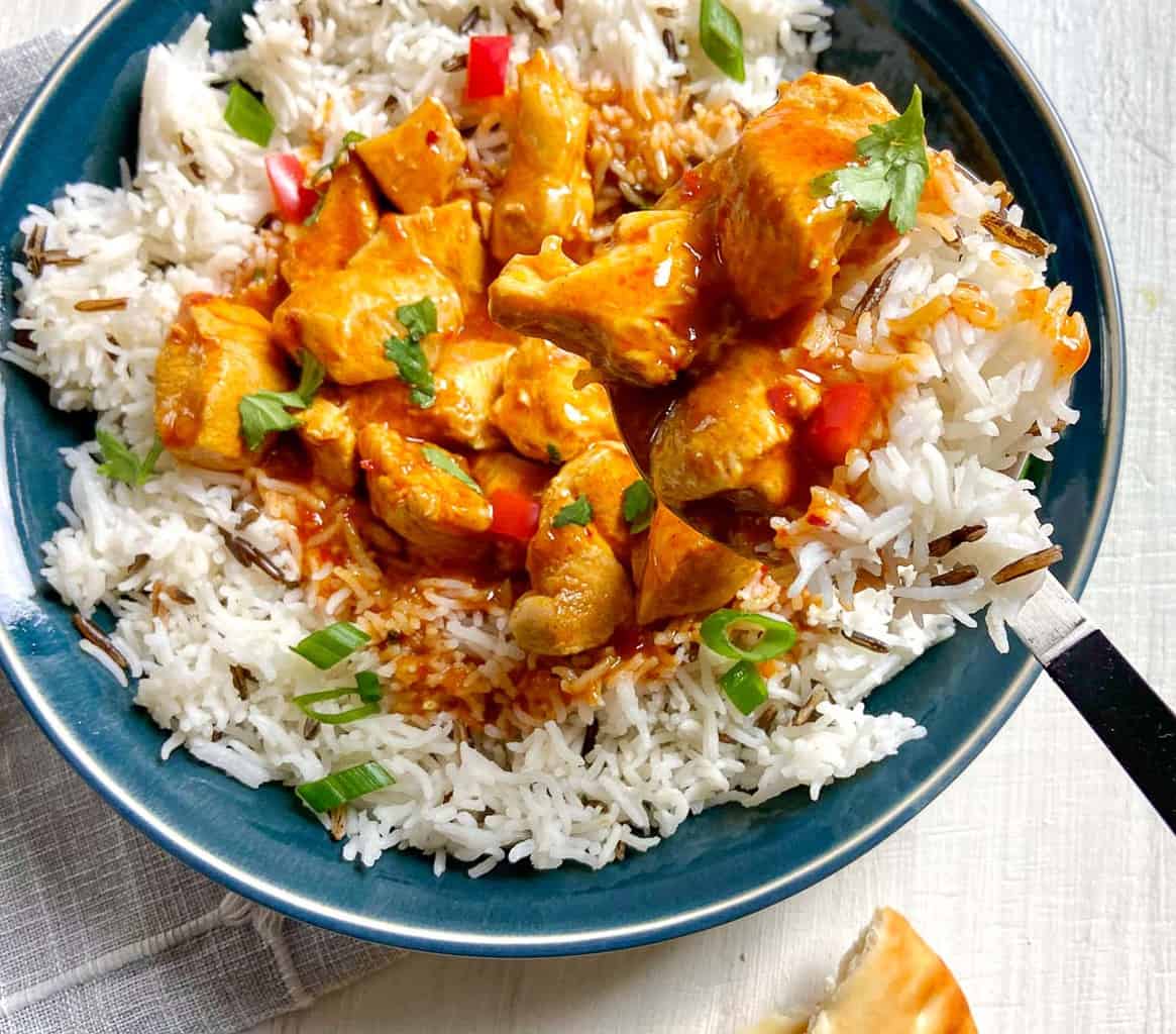 Indian Butter Chicken with basmati rice in blue bowl with serving spoon