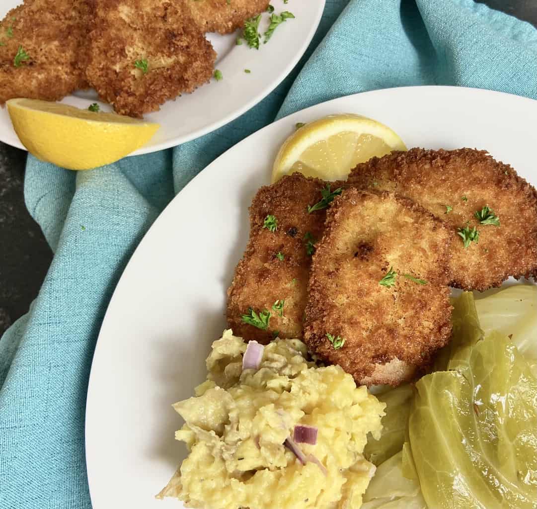 Pork Schnitzel with German potato salad and cabbage on white plate.