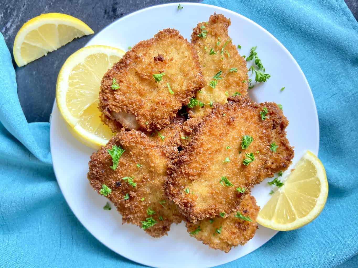 Pork Schnitzel on white plate garnished with parsley and lemon.
