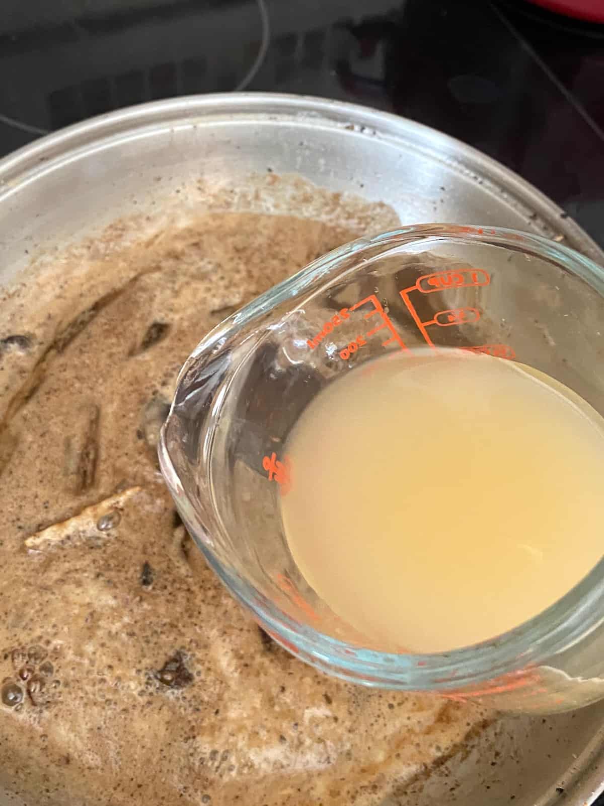 Chicken broth being added to skillet containing roux.