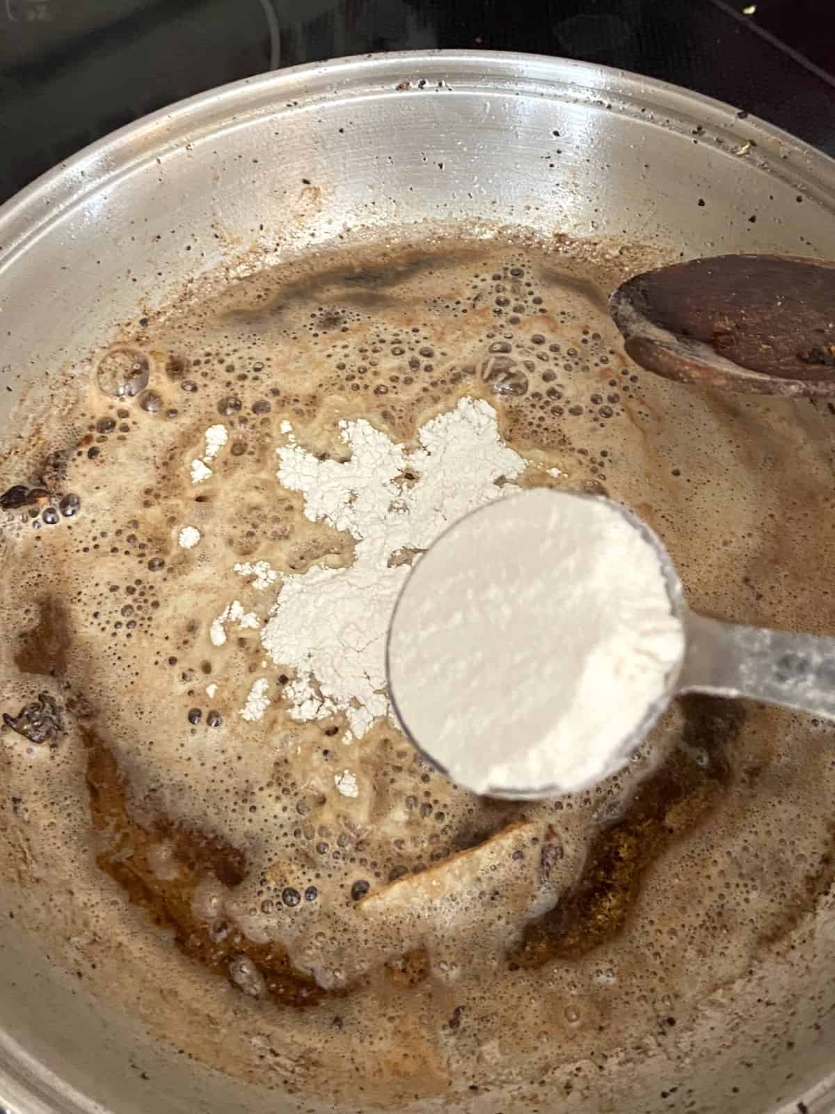 Tablespoon of flour being sprinkled over skillet with bacon grease.