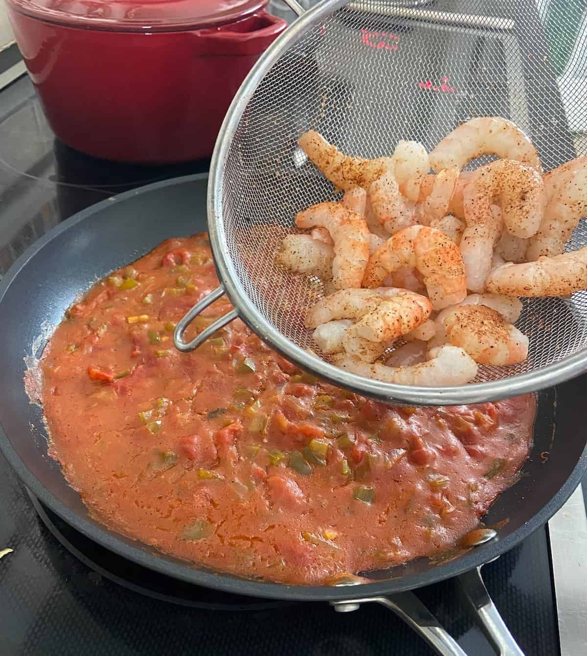 Creole seasoned raw shrimp being added to Creole sauce in skillet.