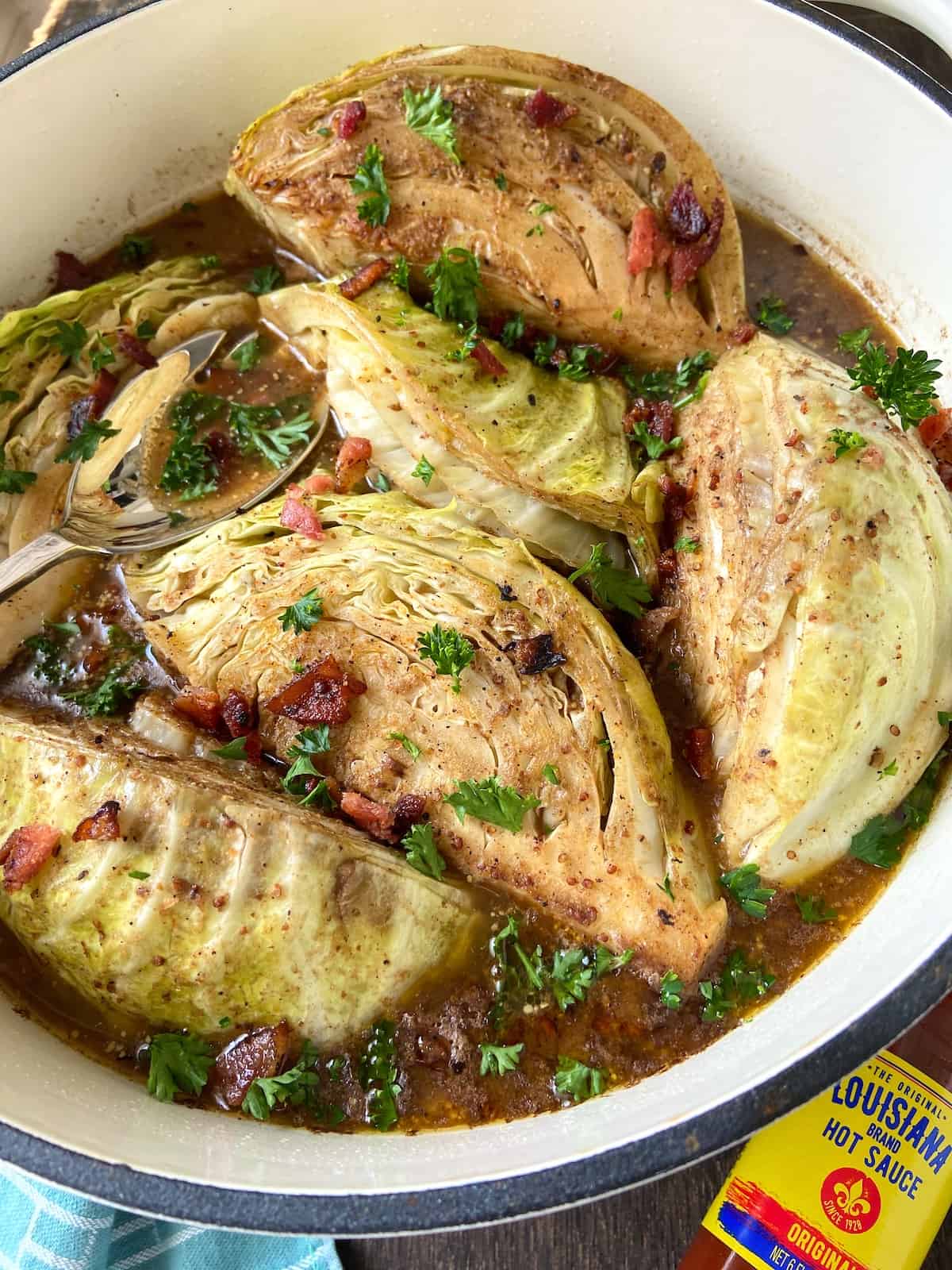 Braised cabbage in Dutch oven garnished with bacon bits and parsley.