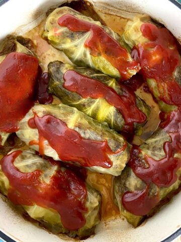 Cabbage rolls in Dutch oven topped with tomato sauce.
