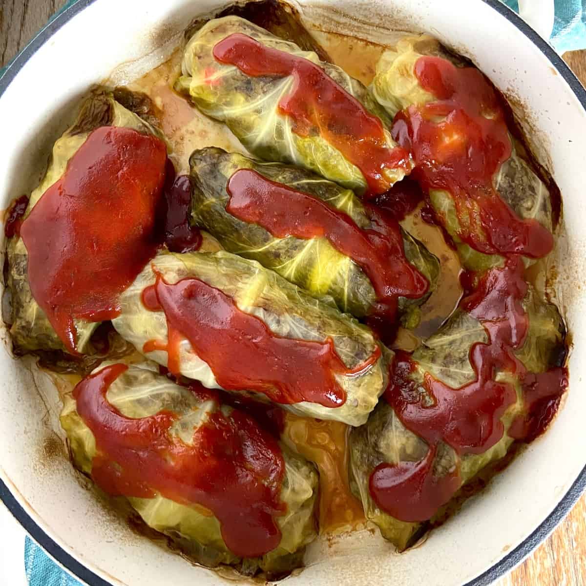 Cabbage rolls in Dutch oven topped with tomato sauce.