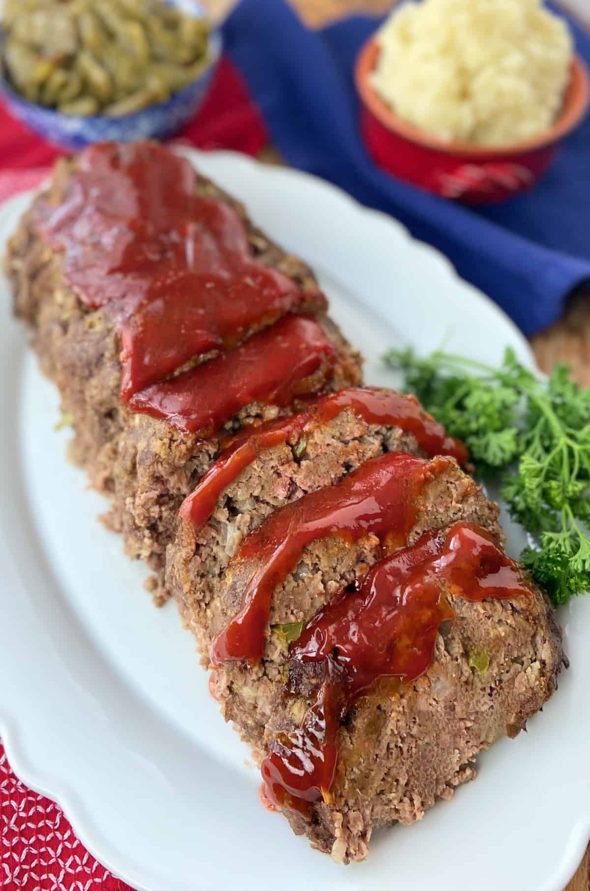 Sliced meatloaf with tomato sauce on white serving platter.