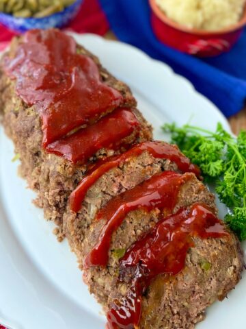 Sliced classic meatloaf with tomato sauce on white serving platter.