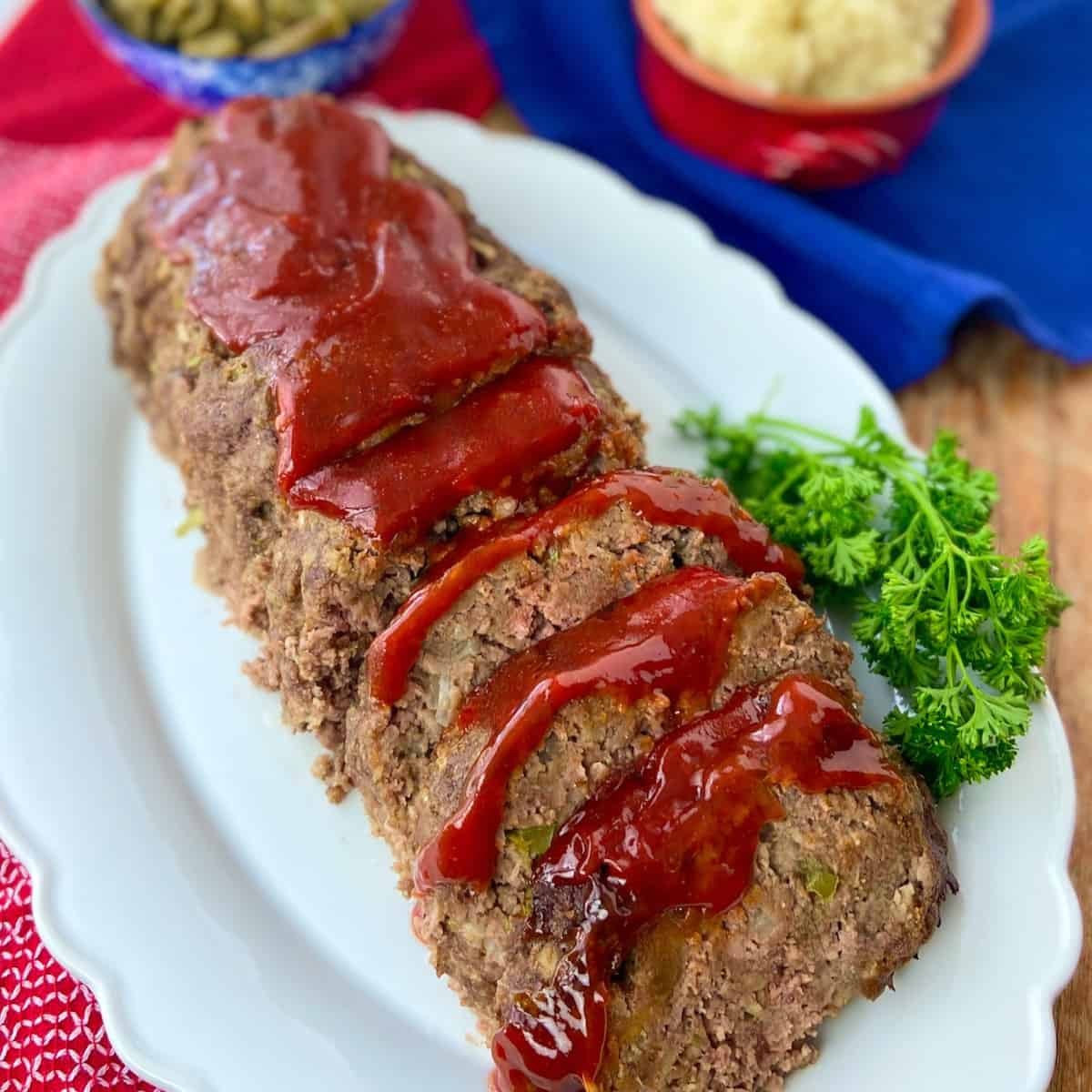 Sliced classic meatloaf with tomato sauce on white serving platter.