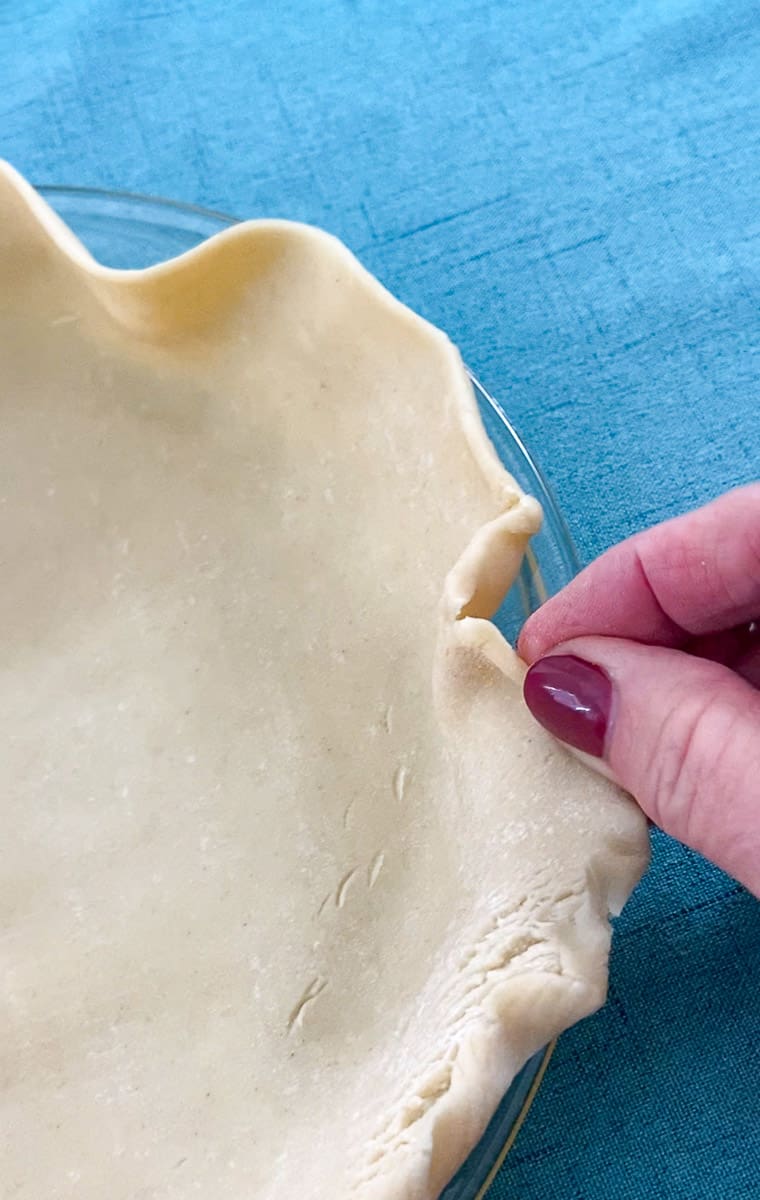 Pie dough pressed into pie plate and edges being crimped