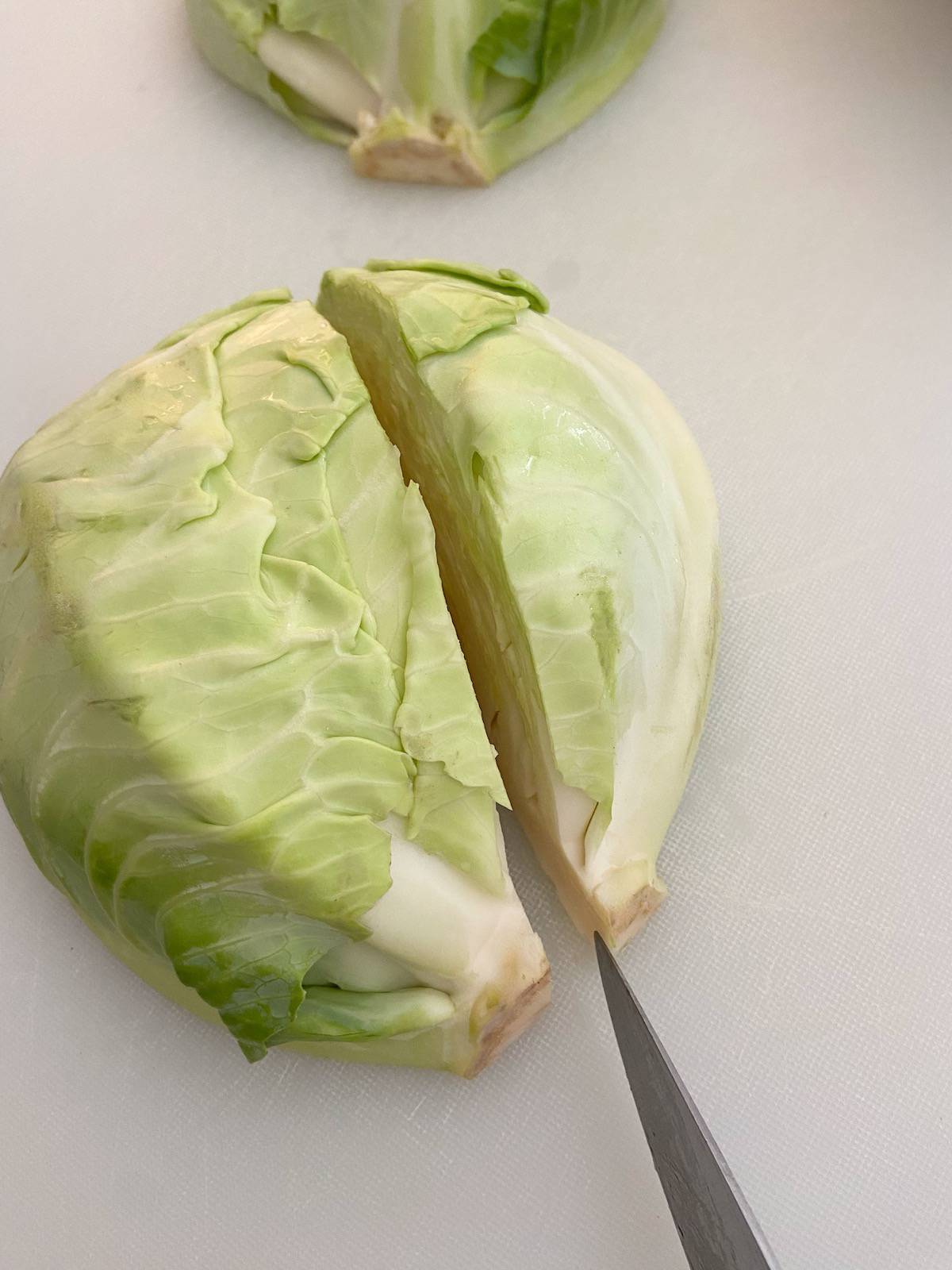 Head of cabbage cut in half on white cutting board.