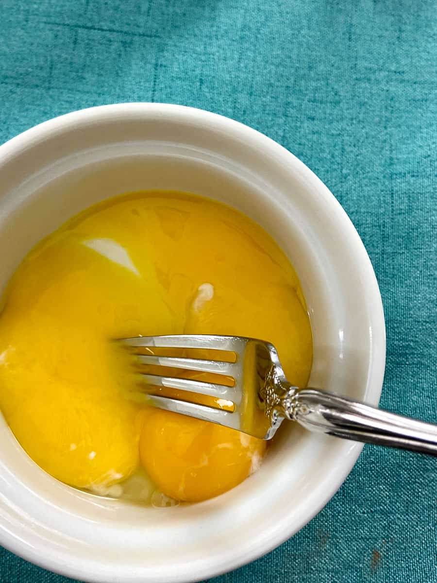 Egg yolks in white ramekin with fork