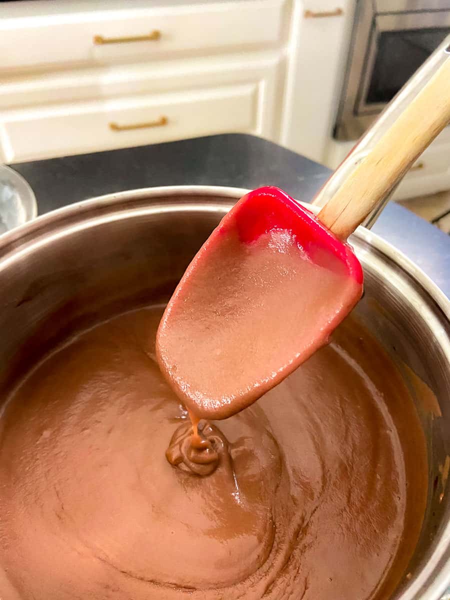 Chocolate pie filling in saucepan sticking to a red spoon