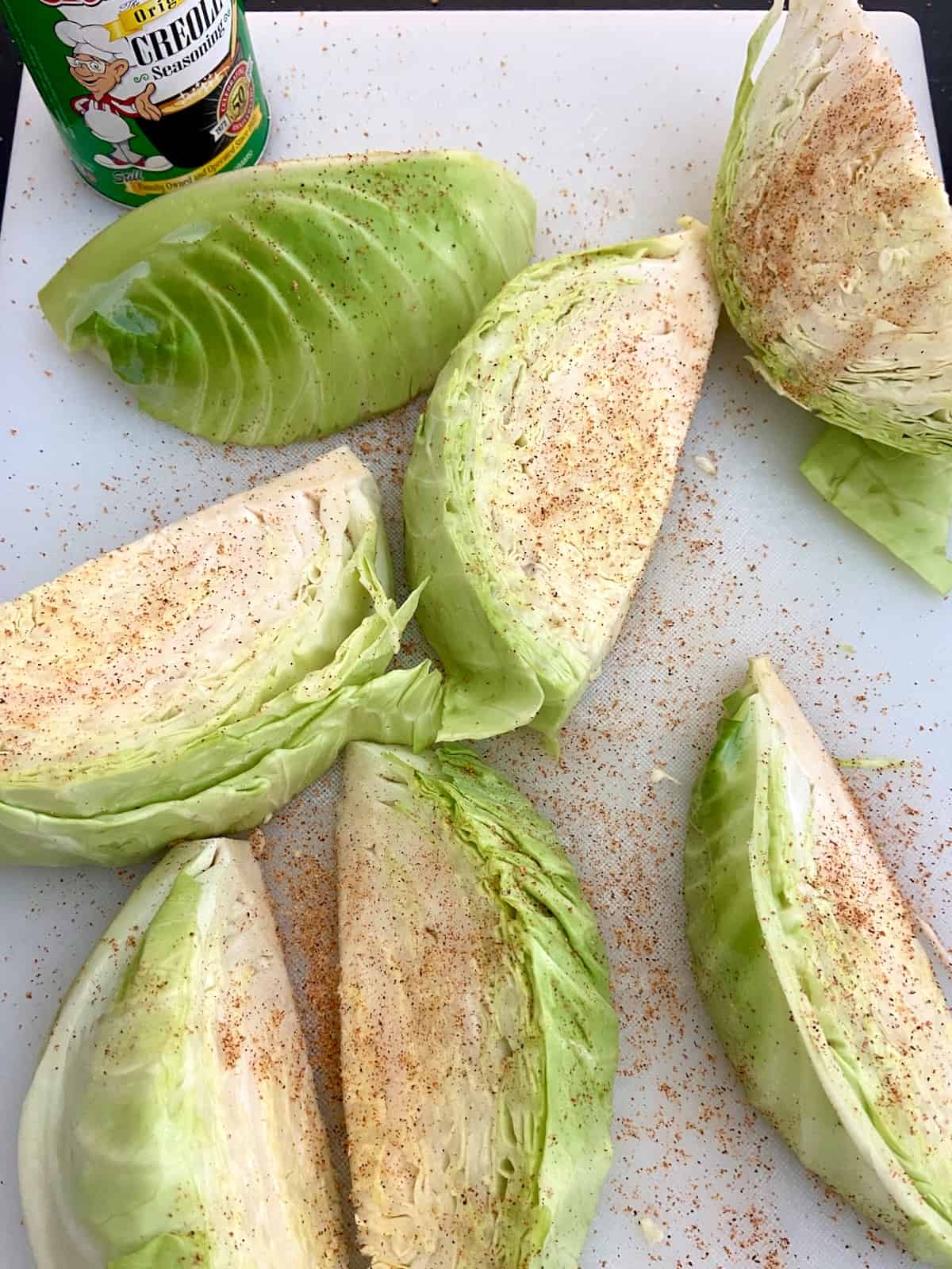 Seasoned cabbage wedges on a white cutting board.