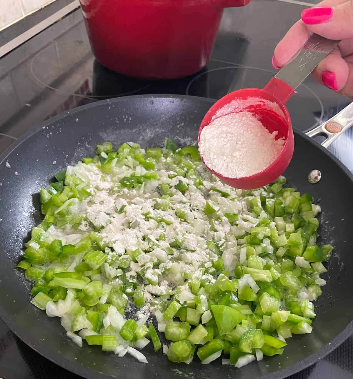 Flour being added to vegetables in skillet.